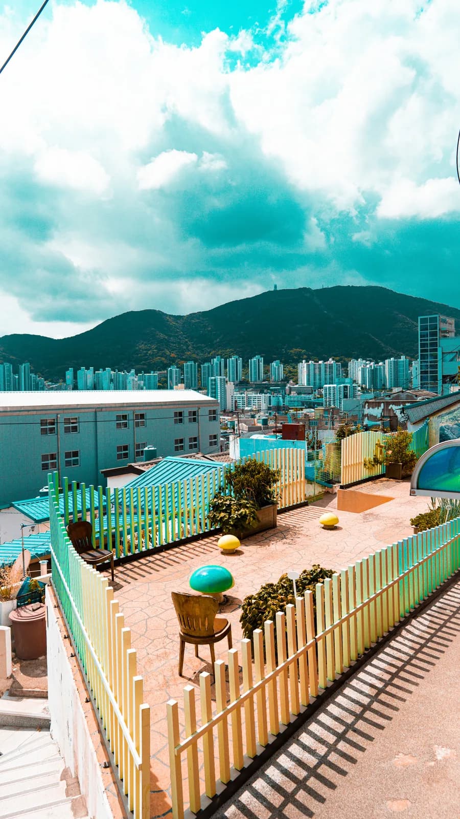 Una terrazza con recinzioni colorate e sedute affacciata sui palazzi e sulle colline di Busan