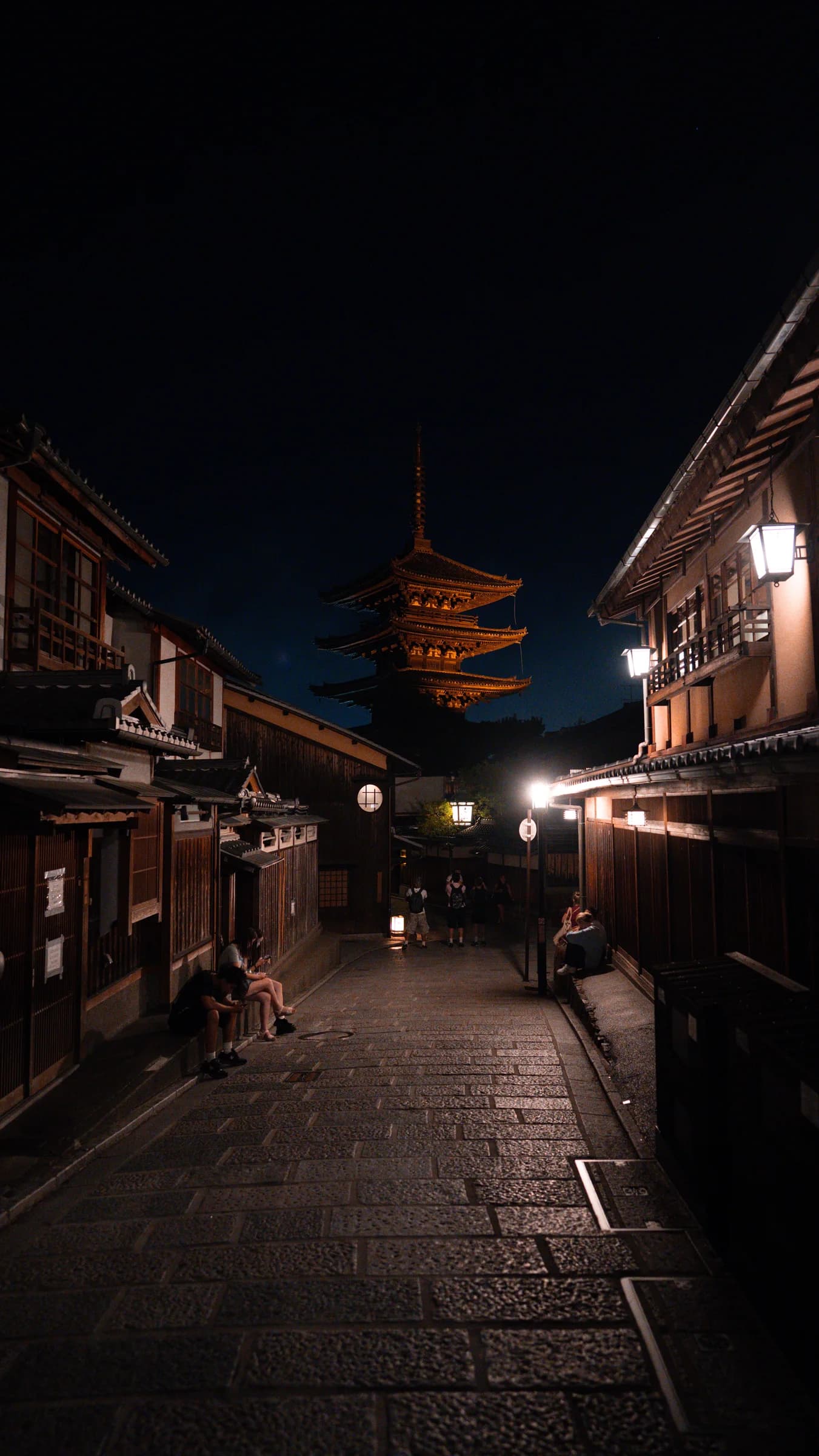 A paved Kyoto street at night, lined with wooden buildings and an illuminated pagoda