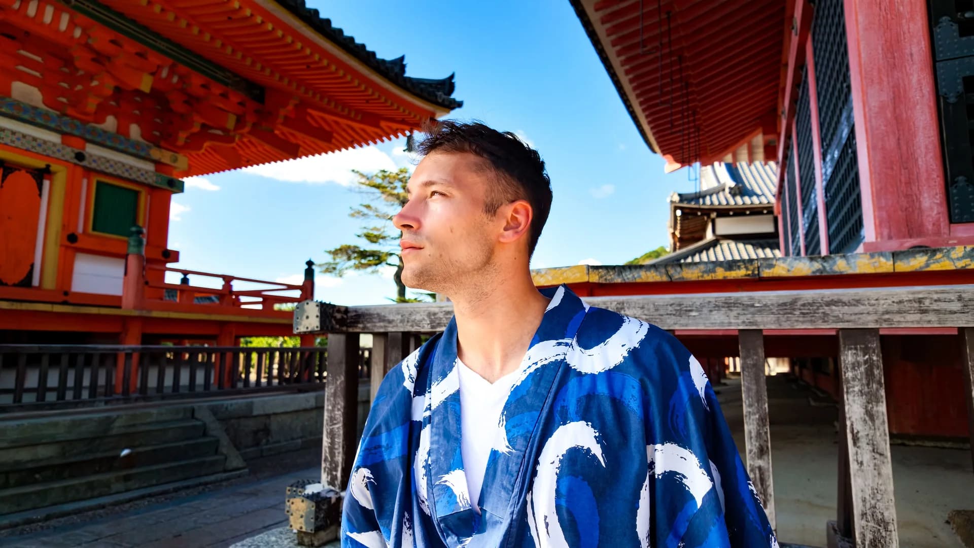 A traveller in a blue and white robe between red-painted wooden buildings