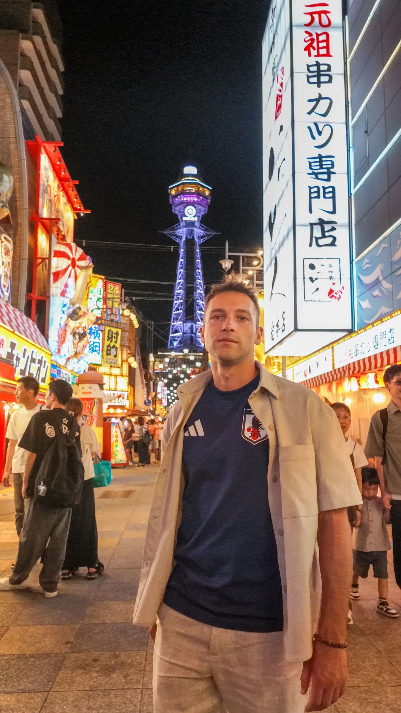 A traveller among Osaka’s illuminated signs, with Tsutenkaku Tower behind him